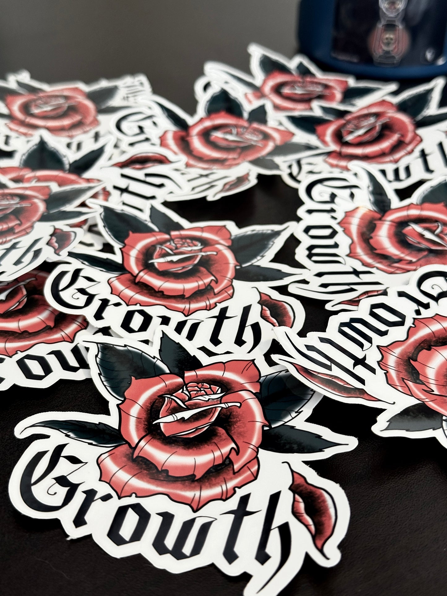 close up of several 3x3 inch die cut stickers with a design of a rose with a fallen petal and gothic calligraphy word "growth". Branded with Rugged Attitude logo.