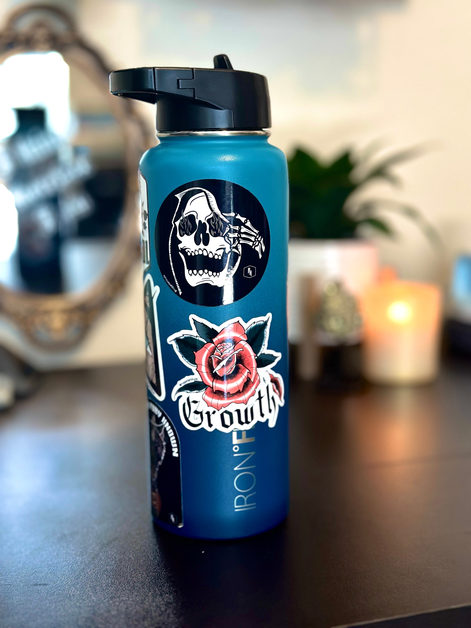 3x3 inch die cut sticker displayed on water bottle in an aesthetic office desk with a design of a rose with a fallen petal and the gothic calligraphy word "growth". Branded with Rugged Attitude logo and paired with several other branded stickers.