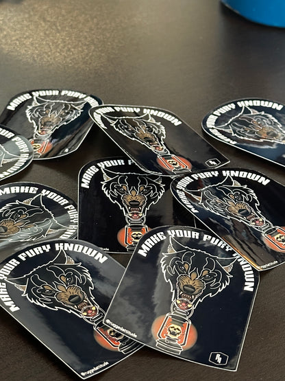 several 2x3 inch die cut stickers laid out on desk, with the design of a wolf holding a lantern and gothic calligraphy words "make your fury known". Branded with Rugged Attitude logo.